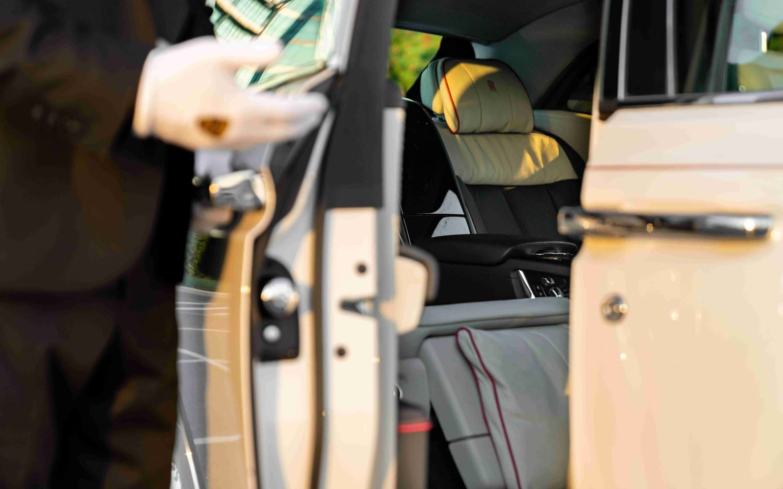 Chauffeur in white gloves opening the rear door of a Rolls-Royce with cream leather interior